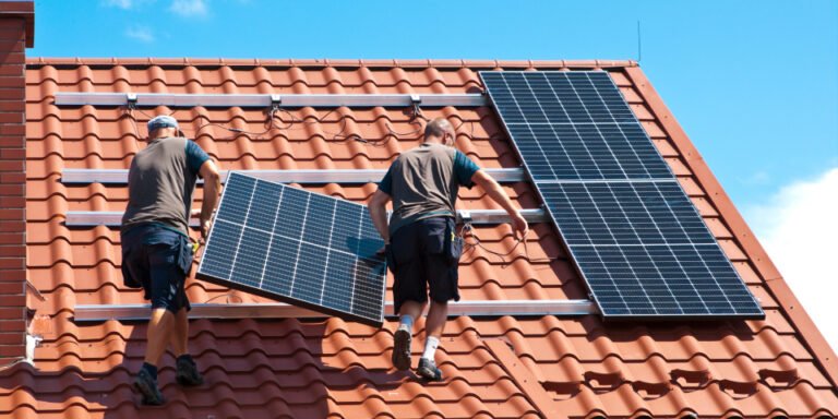 Two workers on a roof, carefully installing solar panels to promote renewable energy solutions.